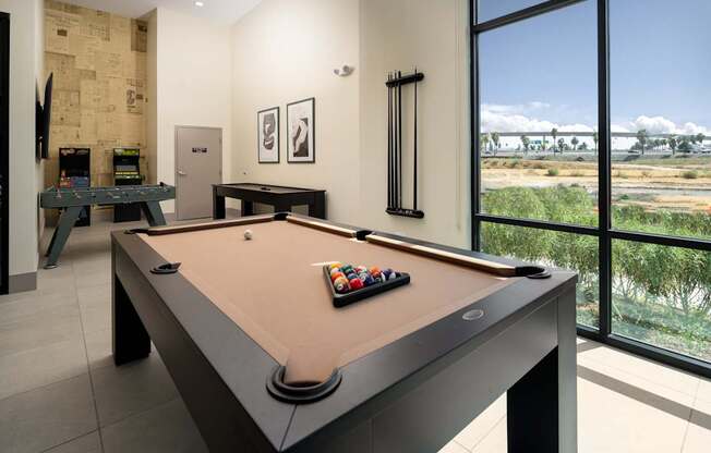 A pool table in a room with a view of the outdoors.
