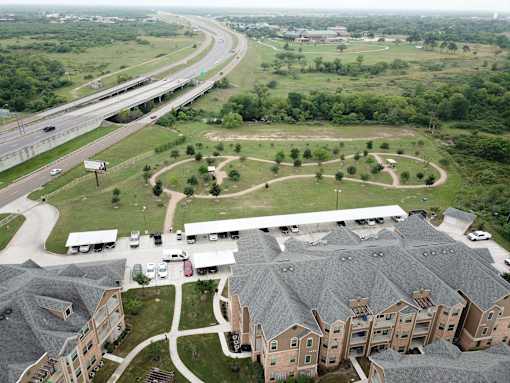 A highway curves through a green landscape with a parking lot and apartment buildings.