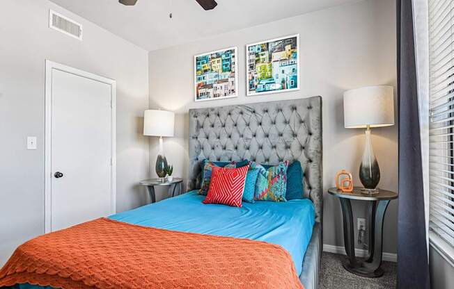 A bedroom with a blue bedspread and a grey tufted headboard.