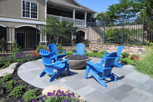 a patio with blue chairs and a fire pit in front of a house