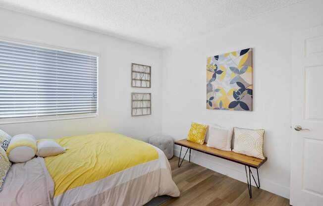 A bedroom with a bed, bench, and artwork at Verandas Apartments, West Covina, California