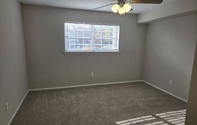 A room with a ceiling fan and a window with blinds.