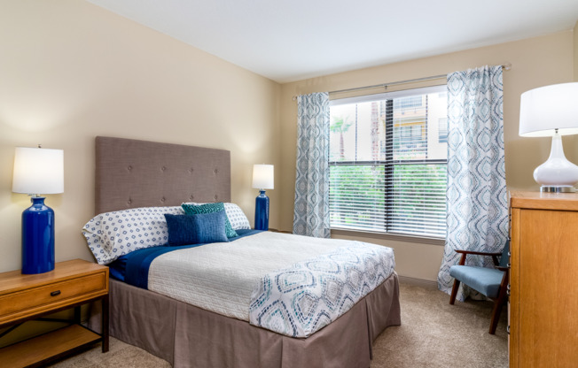 Large windows bring lots of natural light into spacious apartment bedroom with beige carpeting