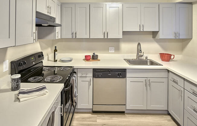 Updated kitchen with stainless steel oven, hood vent, dishwasher and sink from left to right. White countertops and white cabinets. Wood style flooring. at 3030 Lake City, Seattle, WA