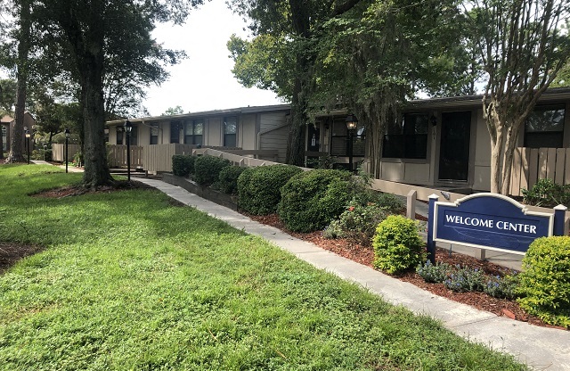 A Welcome Center sign is in front of a building with trees and bushes.