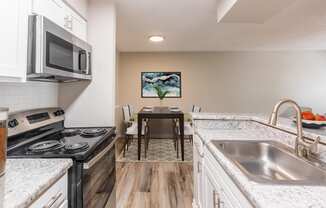 a kitchen with white cabinets and granite countertops and a wooden dining room table with white chairs