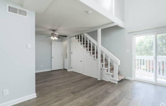 A spacious room with a staircase and a ceiling fan.