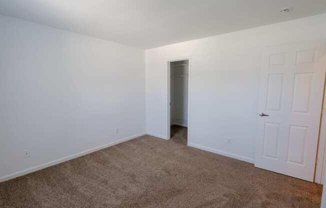 a bedroom with white walls and carpet and a door to a closet
