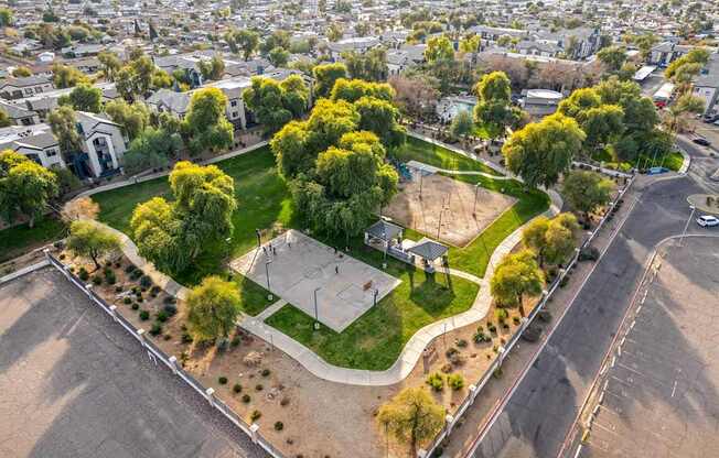 A basketball court is surrounded by trees and grass in a park.