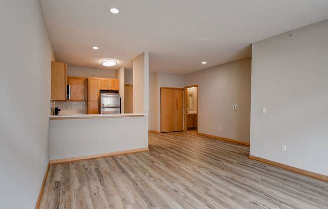 an empty living room with wood flooring and a kitchen