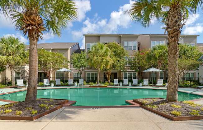 a swimming pool with palm trees and a building in the background at Summerwind, Pearland, TX 77584