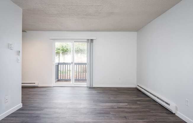 an empty living room with white walls and a door to a balcony