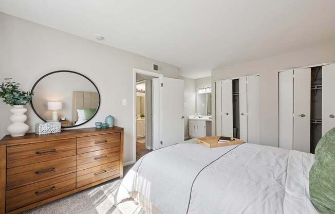 A bedroom with a large bed, a dresser with a mirror, and a green pillow.