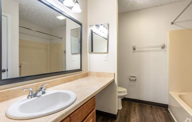 A bathroom with a sink, mirror, toilet and bathtub.