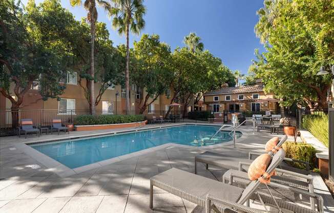 A pool surrounded by palm trees and lounge chairs.