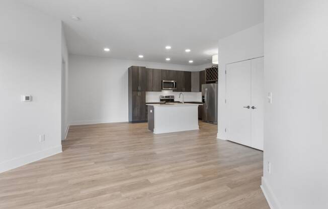 an empty living room and kitchen with white walls and wood flooring