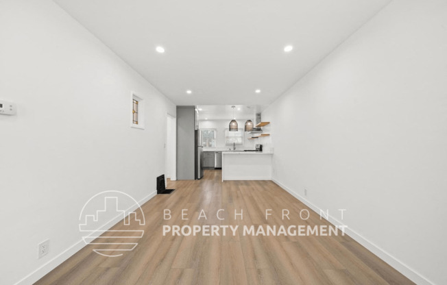 a renovated living room and kitchen with white walls and wood floors