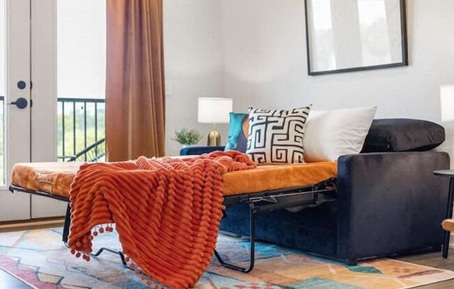 A black sofa with a red throw on it.