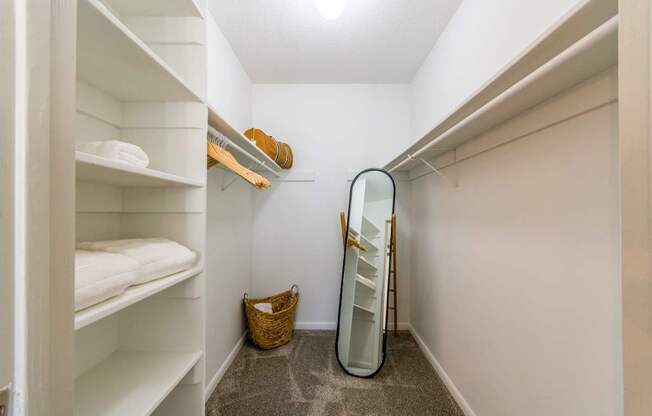 A small, white closet with a mirror and a basket on the floor.