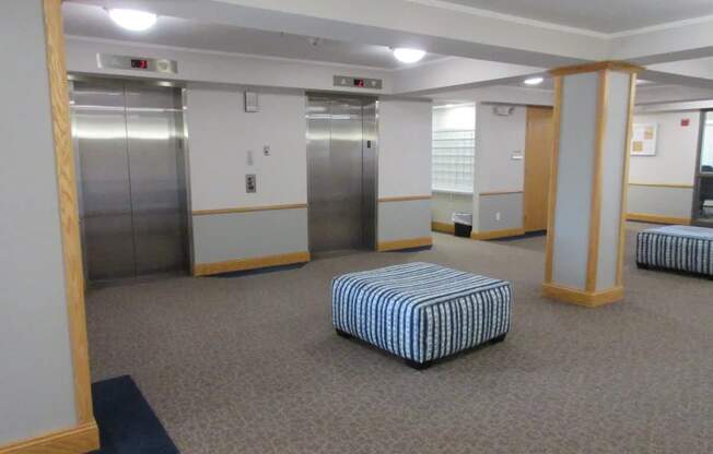 A room with a striped ottoman and two elevators.
