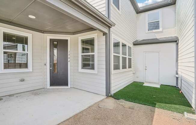 the front entrance of a white house with a porch and grass