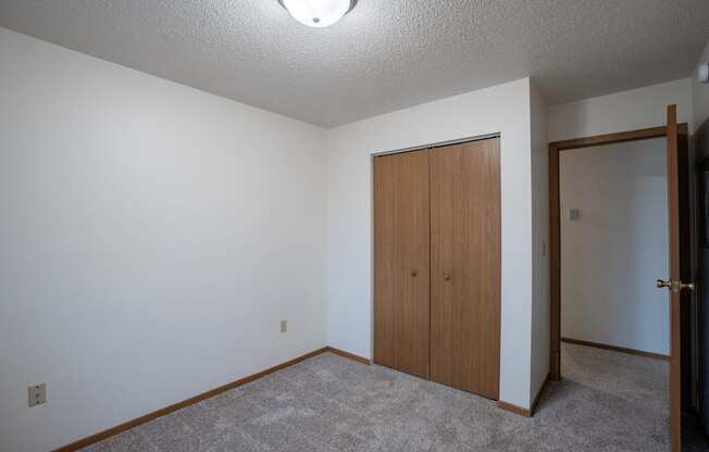 a bedroom with a door to a closet and a carpeted floor. Fargo, ND  Prairie Park Apartments