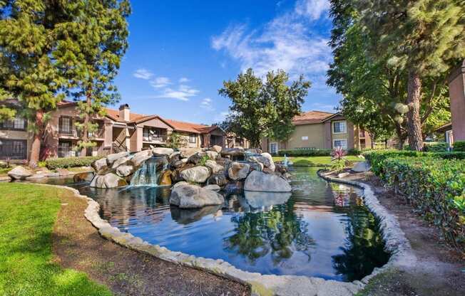 a fountain in the middle of pond surrounded  a grassy area with buildings in the background  at Citrine Hills, Ontario, CA, 91761