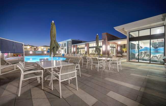 The swimming pool lounge area with tables, chairs and umbrellas at night.