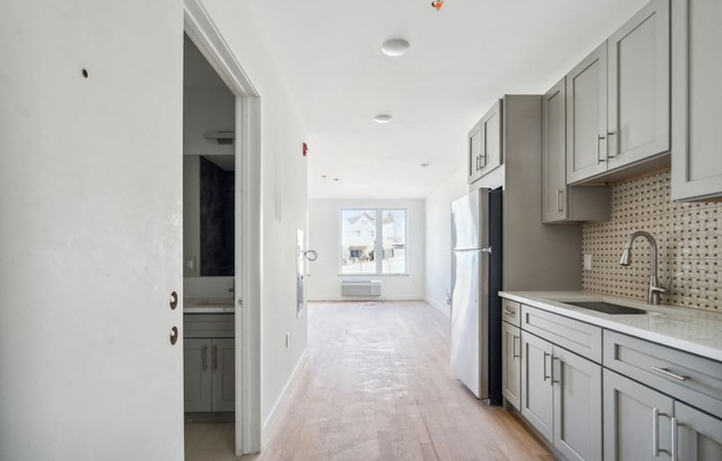 a renovated kitchen with white cabinets and white appliances and a hallway to the living room