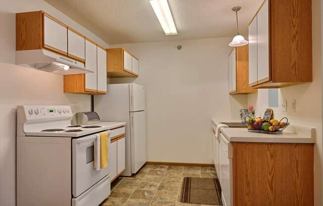 A kitchen with white appliances and wooden cabinets and a white refrigerator. Fargo, ND Eagle Run Apartments
