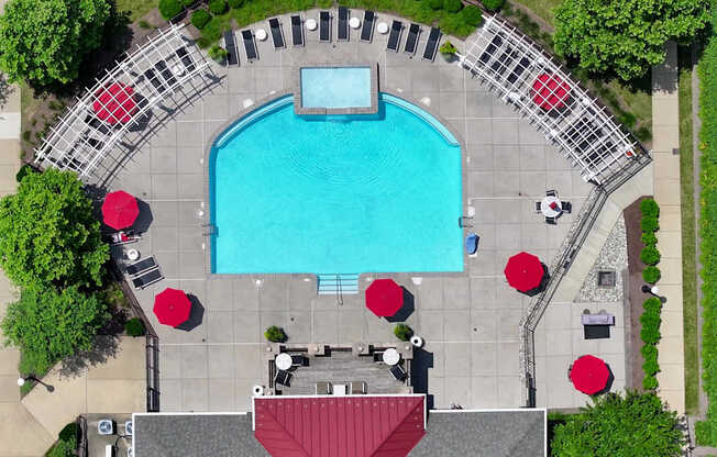 An aerial view of a swimming pool surrounded by red umbrellas and lounge chairs.