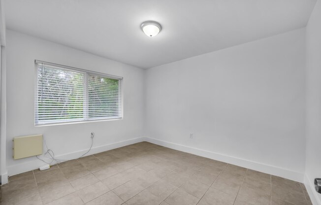 an empty living room with a window and a tiled floor