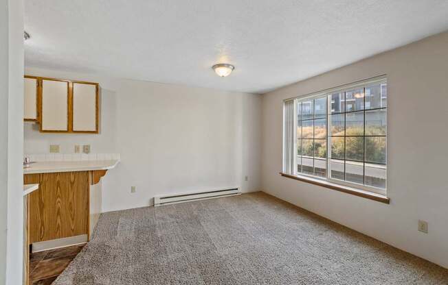 an empty living room with a large window and a kitchen