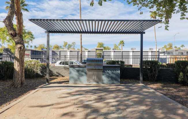 A bus stop with a metal roof and a trash can in front of it.