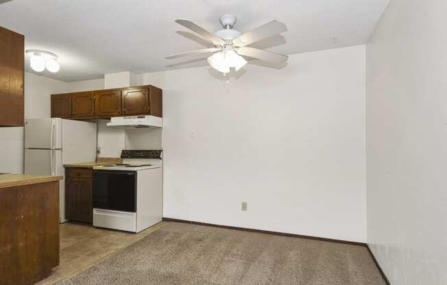 an empty kitchen with a ceiling fan and a white refrigerator. Fridley, MN Georgetown on the River Apartments