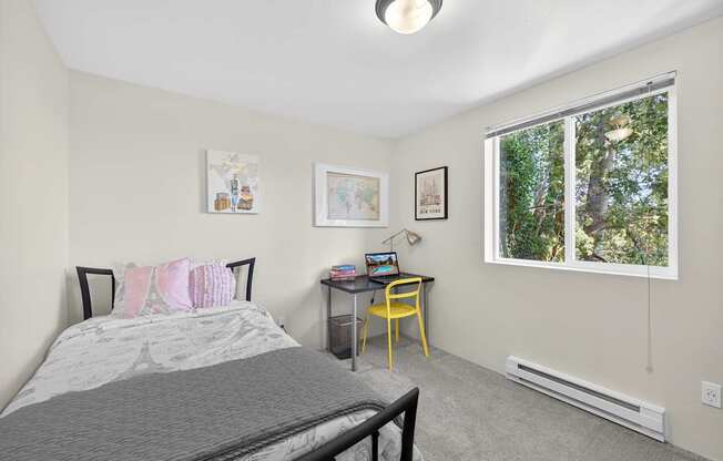 A bedroom with a bed, desk, chair, and pictures on the wall.