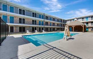A swimming pool is surrounded by sun loungers in front of a building.