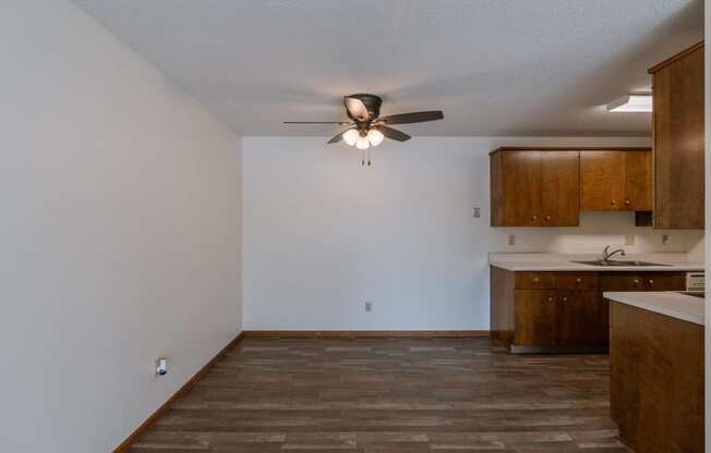 an empty living room with a ceiling fan and a kitchen. Fargo, ND Windsor Apartments