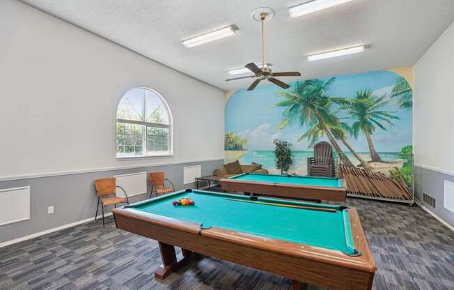 A pool table in a room with a mural of a beach scene on the wall.