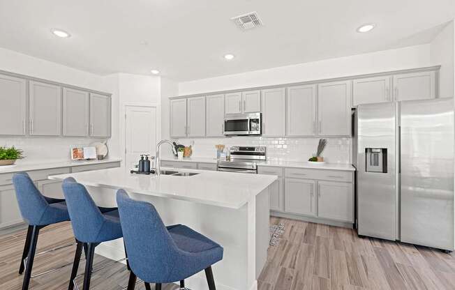 A modern kitchen with a white island and blue chairs.