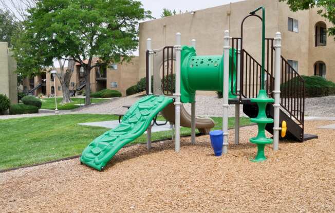 a playground with a green slide in front of a building