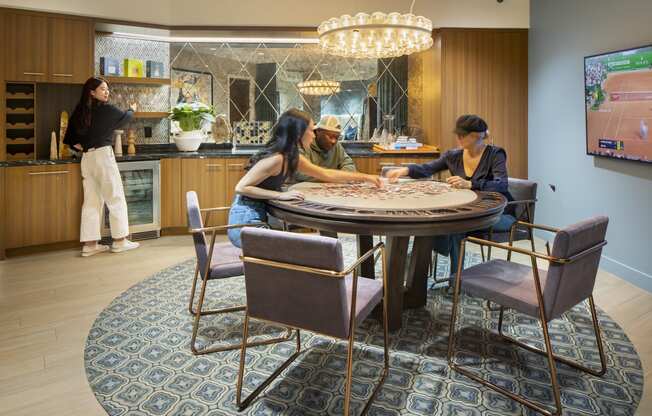 a round table with three people sitting around it and a woman standing in a kitchen in the