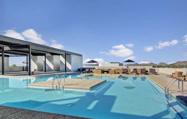 a large swimming pool with lounge chairs and umbrellas on a sunny day