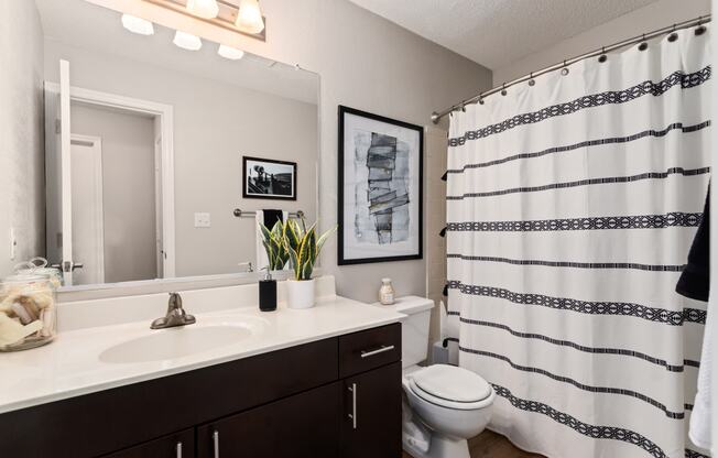 an open bathroom with a white sink and toilet and a black and white shower curtain