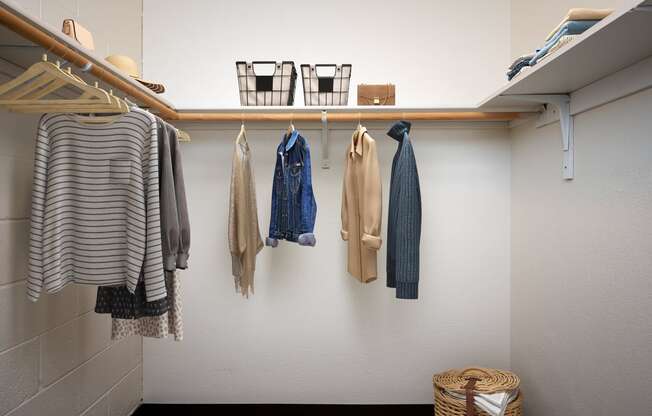 a closet with clothes hanging on the wall and a wooden shelf on the ceiling