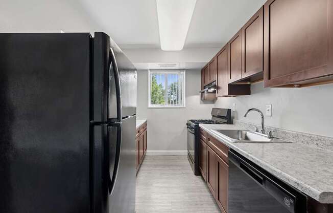 A black refrigerator is in a kitchen with brown cabinets.