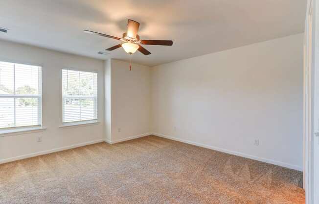 an empty living room with a ceiling fan and two windows