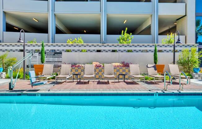 A pool area with a row of chairs and a building in the background.