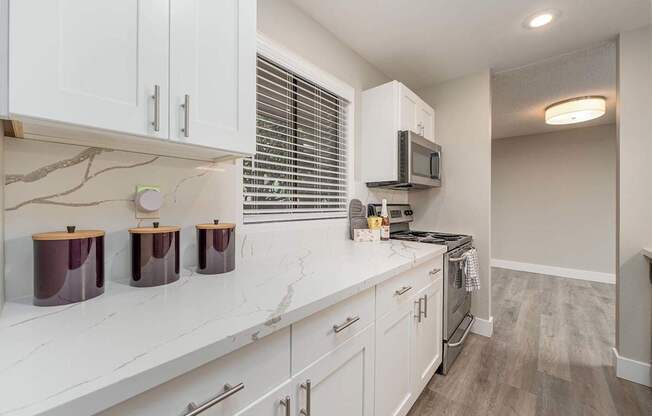 A kitchen with white cabinets and a countertop with three jars on it.