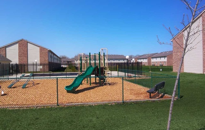 Playground with a slide and monkey bars inside a fenced area at Maple Tree Apartments in LaPorte, IN